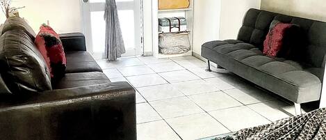 A living room with a sofa, a chair, a bed, a wardrobe, and a television on the wall.
