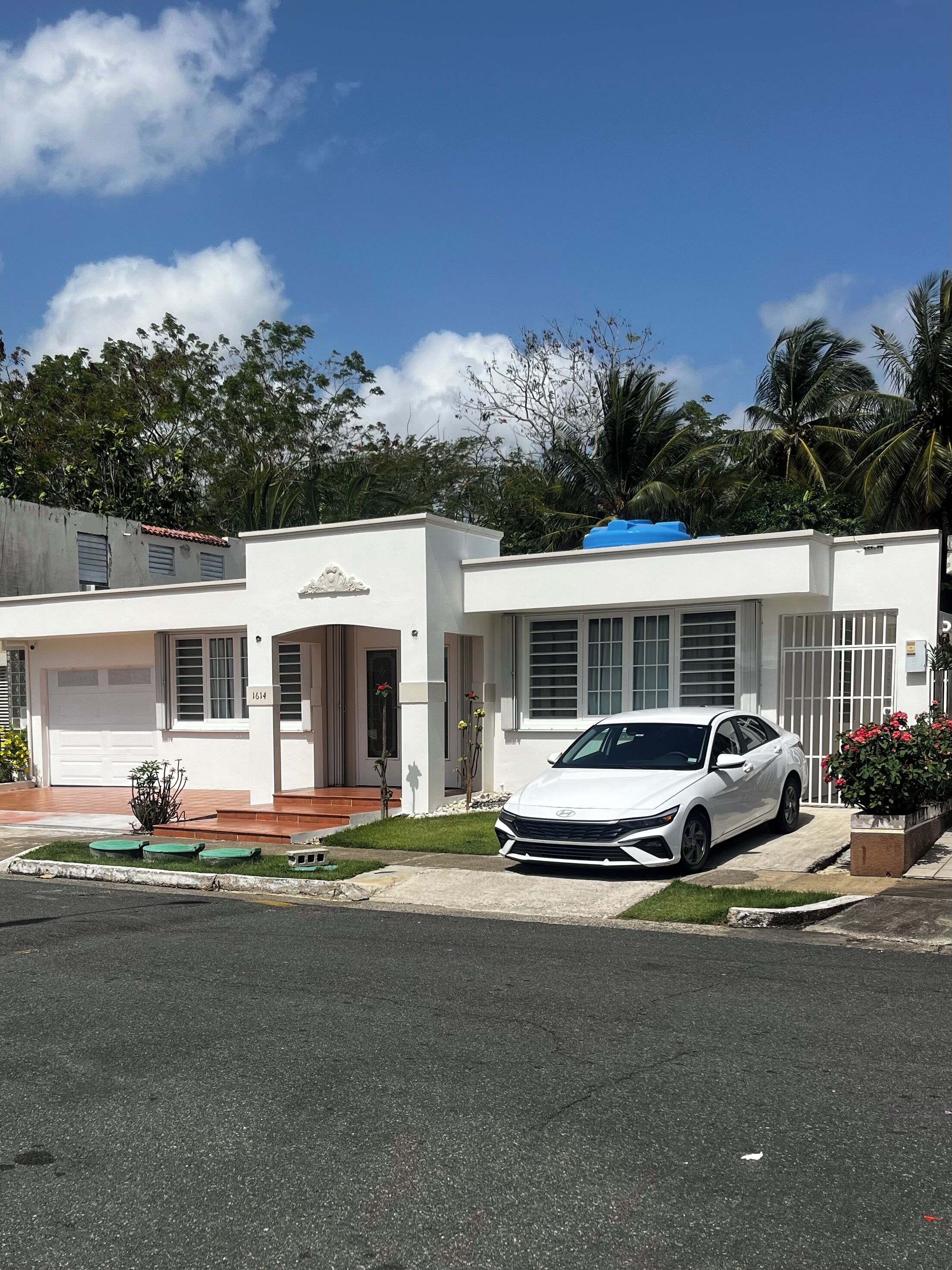A white two-story house with a garage, a driveway, and a white car parked in front.