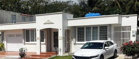 A white two-story house with a garage, a driveway, and a white car parked in front.