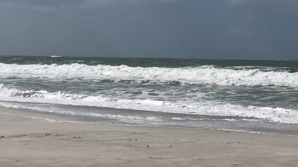 Une plage où les vagues se brisent sur le rivage sous un ciel nuageux.