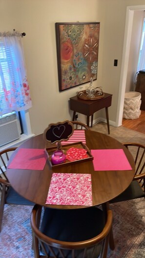 A dining area with a round wooden table, pink placemats, and a decorative mirror with a heart frame. - Charming Cottage Five miles from U of A campus (Fayetteville)
