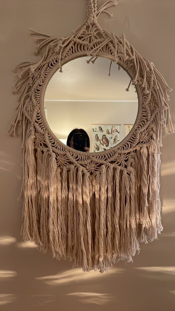 A macramé wall hanging with a circular mirror.