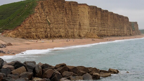Acantilado costero con playa y primer plano rocoso.