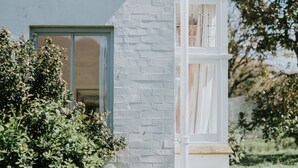 Una casa con fachada de ladrillo blanco, una puerta verde y un ventanal con cortina.