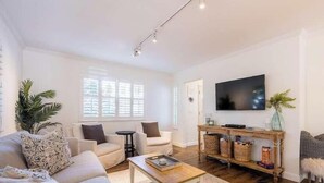 Ein Wohnzimmer mit einer Couch, Sesseln, einem Couchtisch, einem Fernseher und einem Konsolentisch mit Körben.