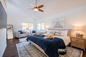 A bedroom with a large bed, a ceiling fan, a nightstand, a lamp, and a window with a view of a dock. - Amazing Beach House w/ Jacuzzi and Fire Pit (Aptos)