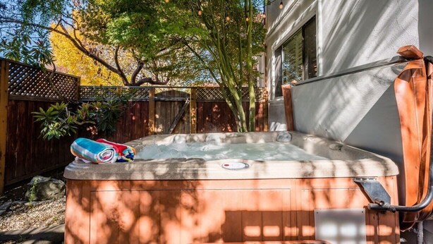 A hot tub with a built-in seat and a step for access, surrounded by a wooden fence and trees. - Amazing Beach House w/ Jacuzzi and Fire Pit (Aptos)