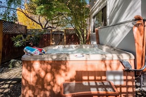 A hot tub in a backyard with a wooden deck, a ladder, and a tree in the background. - Amazing Beach House w/ Jacuzzi and Fire Pit (Aptos)