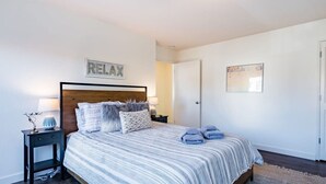 A bedroom with a bed, bedside tables, a nightstand, a wall-mounted artwork, and a door. - Amazing Beach House w/ Jacuzzi and Fire Pit (Aptos)