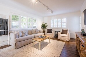 A spacious living room with a sofa, two armchairs, a coffee table, and a TV on a wooden stand. - Amazing Beach House w/ Jacuzzi and Fire Pit (Aptos)