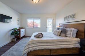 A bedroom with a large bed, a dresser, a potted plant, and a window with a view of trees. - Amazing Beach House w/ Jacuzzi and Fire Pit (Aptos)