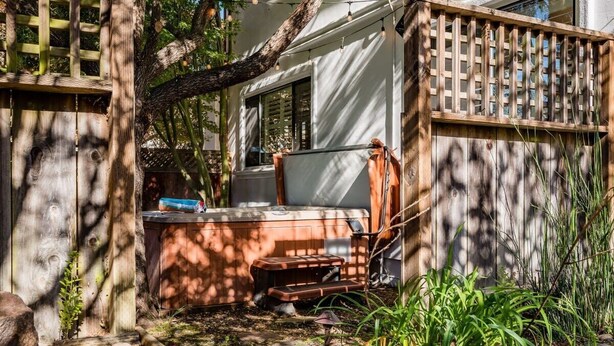 A hot tub in a garden area with a wooden fence, a bench, and a tree.