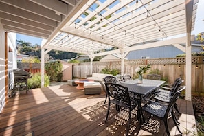 A covered patio with a wooden deck, a table with chairs, a sofa, and a grill. - Amazing Beach House w/ Jacuzzi and Fire Pit (Aptos)