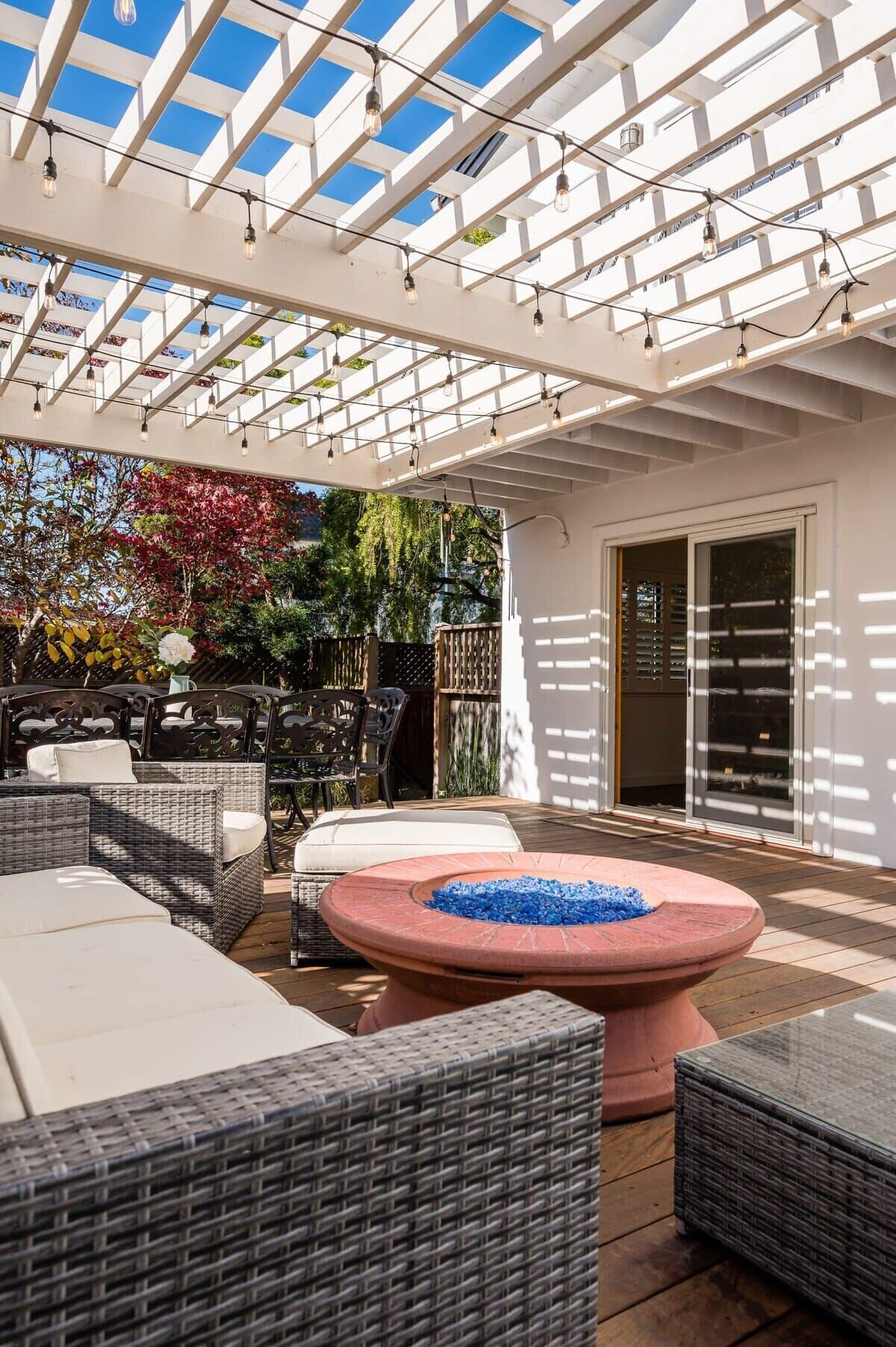 Une terrasse extérieure aménagée avec des meubles en osier, un foyer et une pergola illuminée de guirlandes lumineuses.