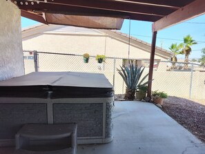 Ein Patio im Freien mit überdachter Sitzgelegenheit, einem Betonboden und einem Zaun aus Maschendraht, der den Bereich begrenzt.