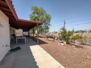 Eine überdachte Terrasse mit Tisch, Stühlen und einer Bank, sowie ein kleiner Baum mit orangefarbenen Blüten.