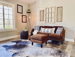 A living room with a brown leather sofa, a patterned rug, and rustic window frames.