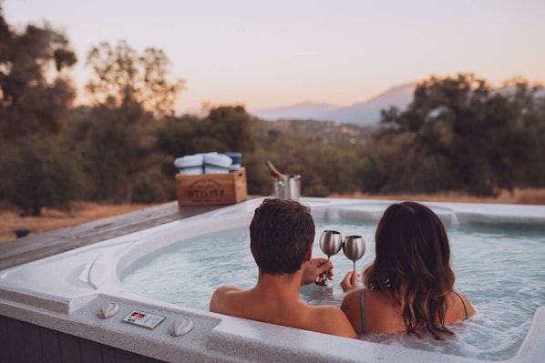 A couple in a hot tub with a view of trees and mountains in the background.