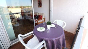 A balcony with a purple table set for two, white chairs, and a glass door leading to an indoor area with a couch and a painting.