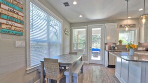 A modern kitchen with a dining area, featuring a wooden table and chairs, a built-in island with a sink, and a view through the window.