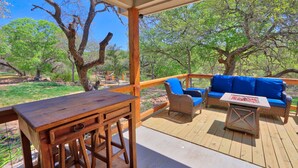 An outdoor deck with a wooden table and chairs, a blue sofa, and a small table with a red and white design.