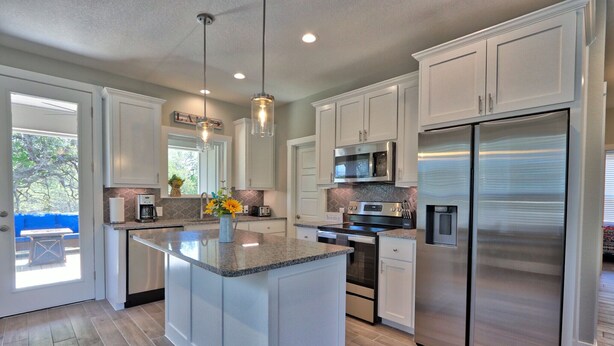 A modern kitchen with white cabinets, a large island, stainless steel appliances, and pendant lighting.