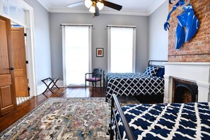 A bedroom with two beds, a fireplace, a ceiling fan, and a large window. - Historic B&B in the Heart of the City (New Orleans)