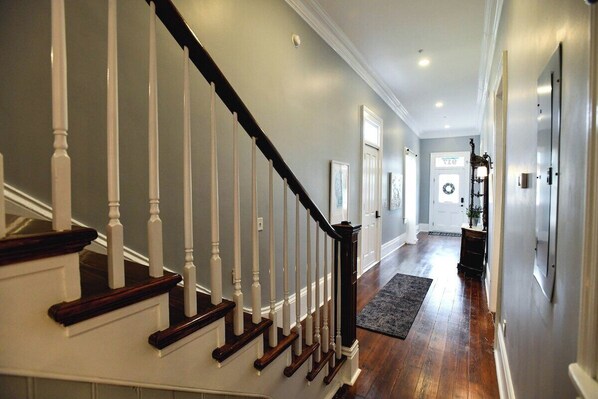 A hallway with a wooden staircase, a rug, and a door with a wreath.