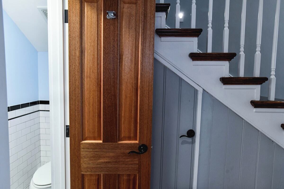 A wooden door with a black handle, a white doorbell, and a white wall with a black stripe.