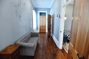 A hallway with a tufted bench, wooden flooring, a door leading to a room, and a wall-mounted light fixture.