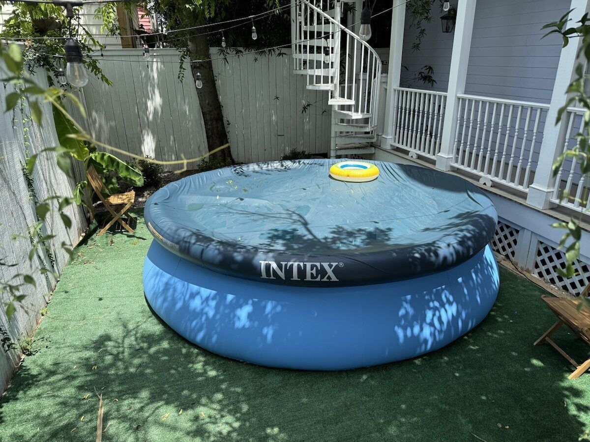 A round inflatable pool with a yellow float on a green surface, surrounded by a white fence and a staircase.