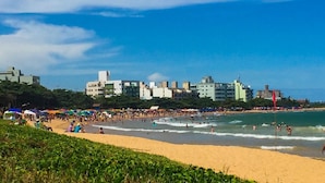 A beach with people, a sandy shore, and buildings in the background. - Pousada Maravista (Anchieta)