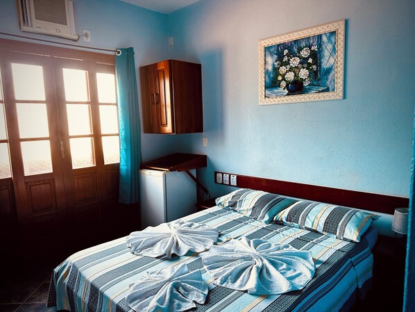 Un dormitorio con cama, una mesita, un armario y un cuadro en la pared.