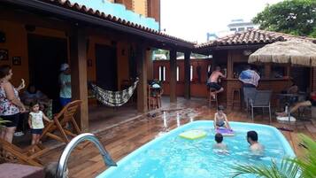 Área de piscina com deck revestido, espreguiçadeiras e estrutura de telhado de palha.