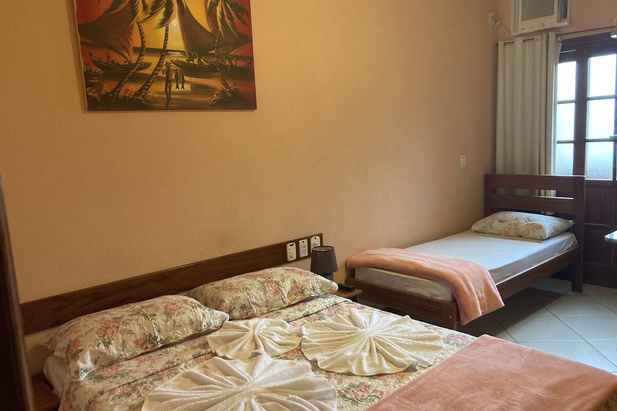 A hotel room with two beds, a painting on the wall, and a window with curtains.