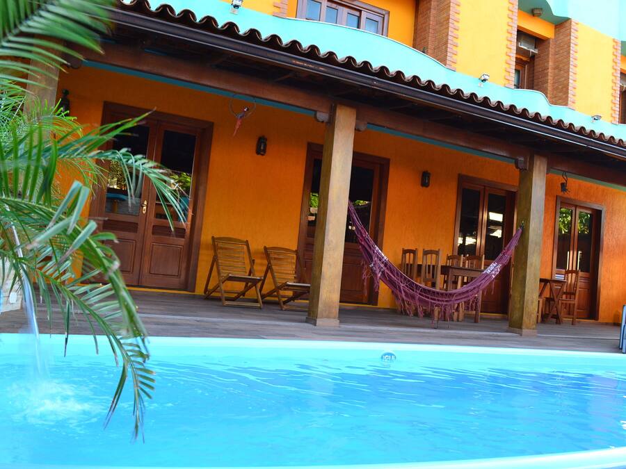 A pool area with a hammock, wooden chairs, and a building with orange walls and a blue roof.