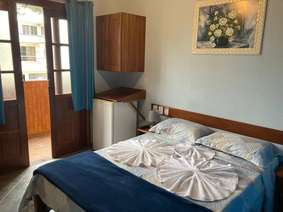 Een slaapkamer met een bed, een klein bureau, een lamp en een schilderij aan de muur.