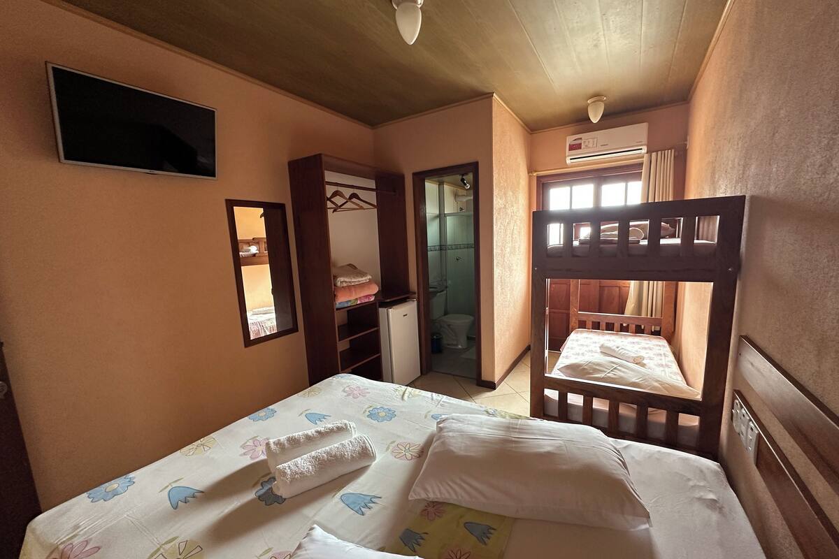 A bedroom with a bunk bed, a wardrobe, a mirror, a television, and an air conditioning unit.