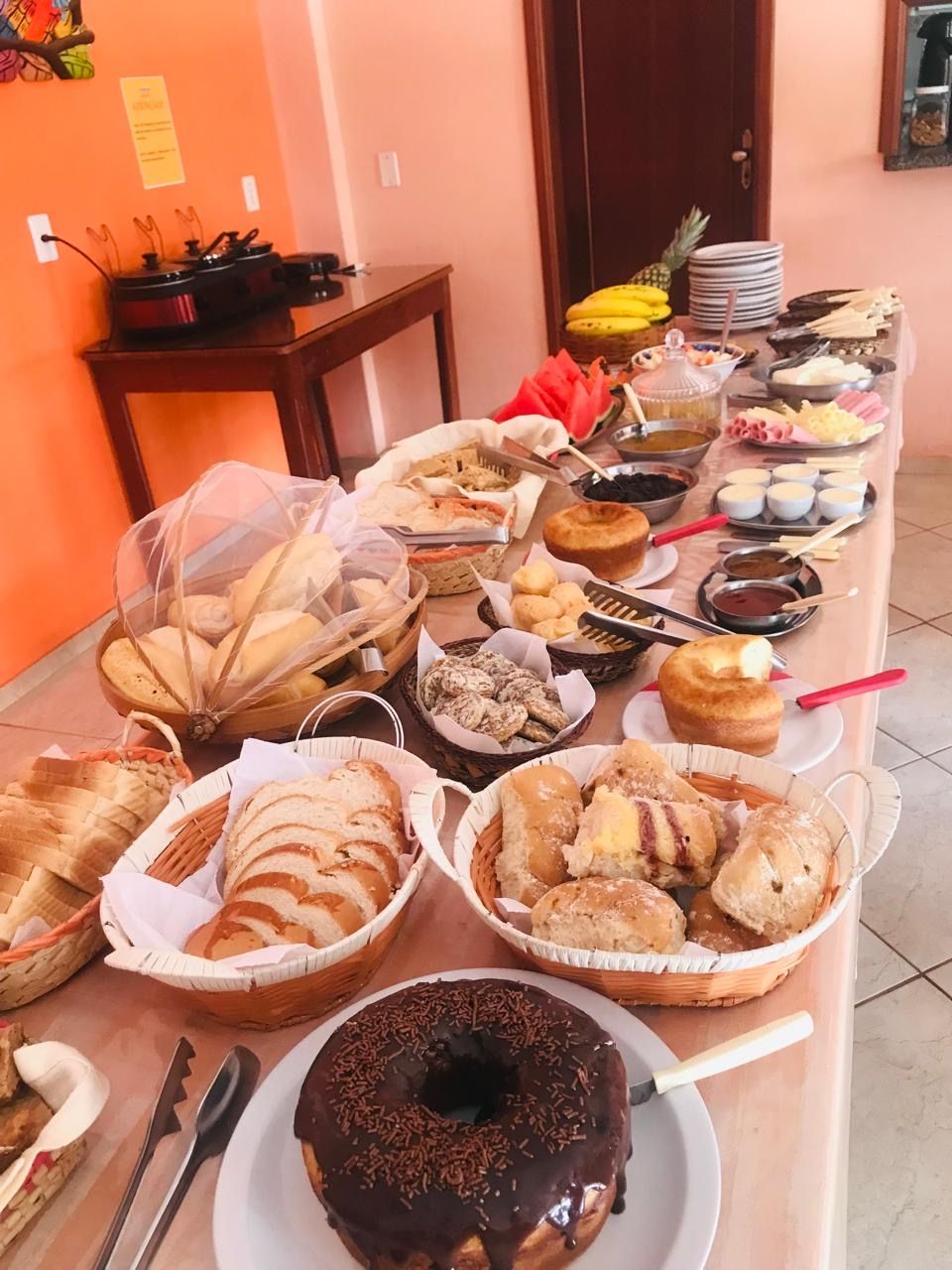 A buffet table with various food items including bread, pastries, and a chocolate-covered donut.