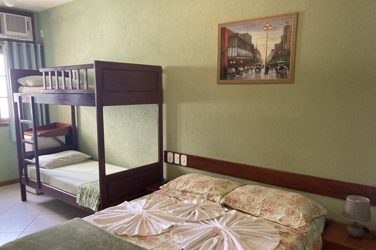 A bunk bed with a ladder, a single bed with floral bedding, a wall-mounted power outlet, and a framed picture of a cityscape.