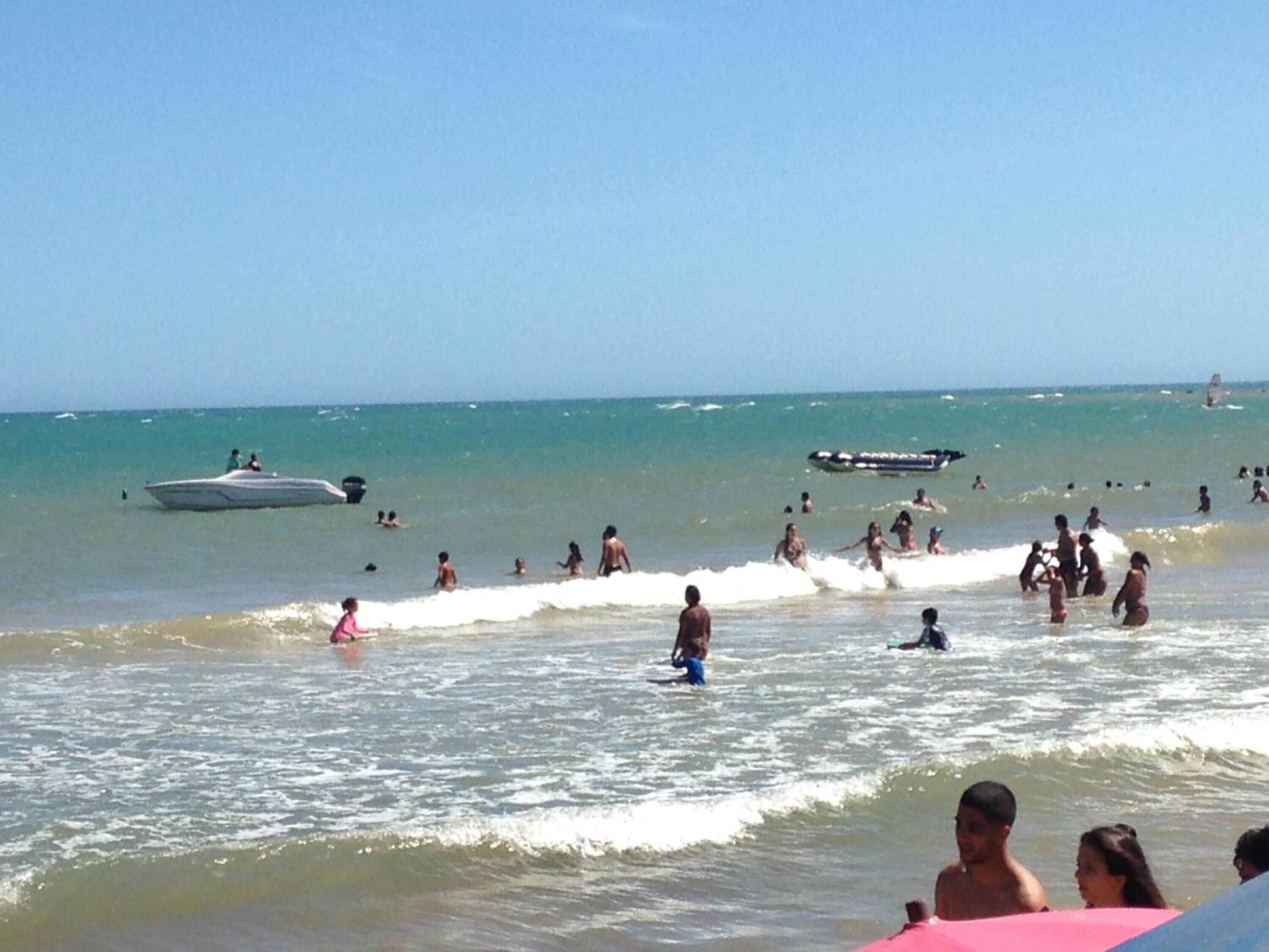 Uma praia com pessoas nadando e um barco na água.