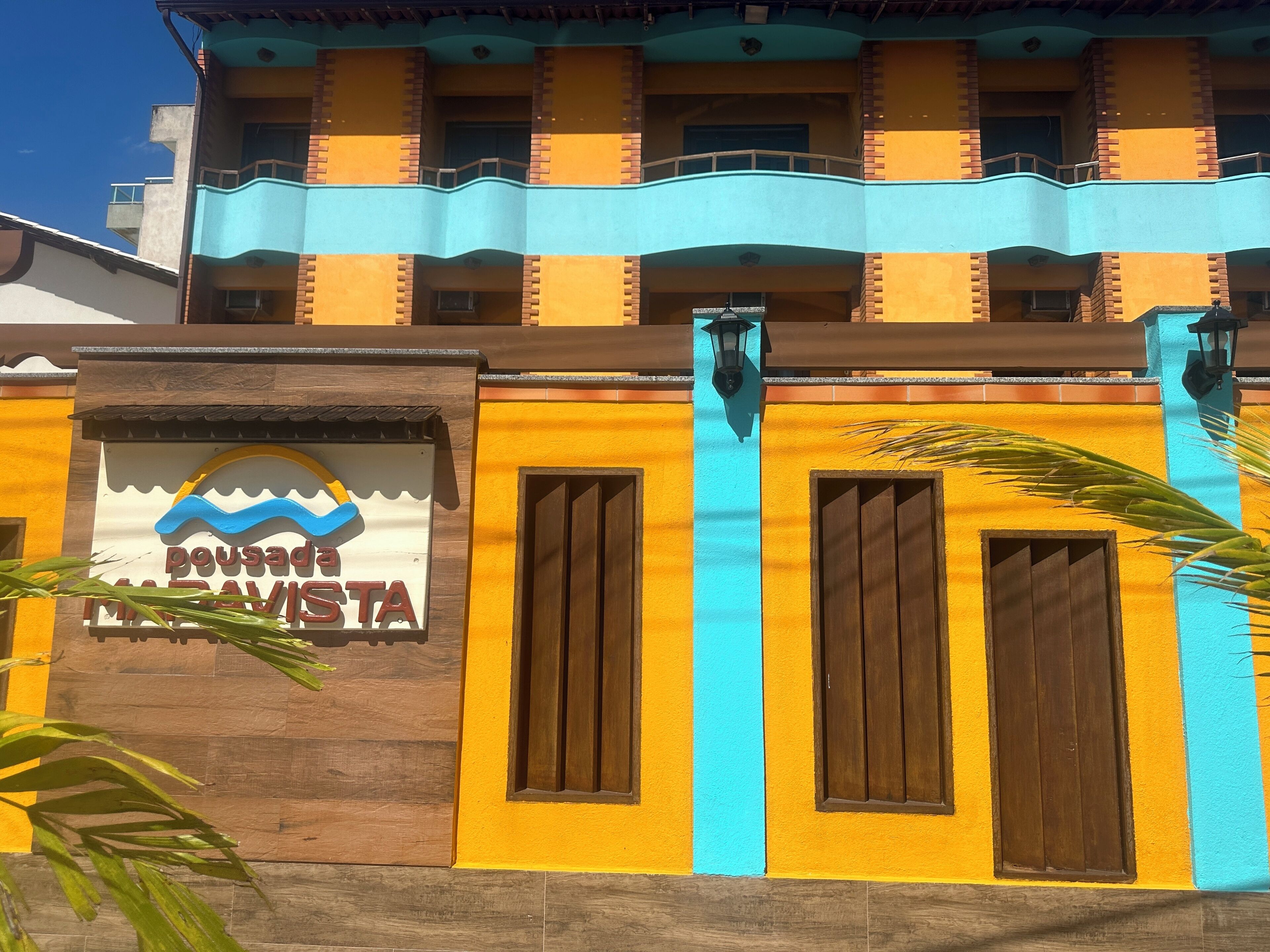 A building with a sign reading "Pousada Ma Davis." It features a yellow facade with blue accents and wooden shutters.