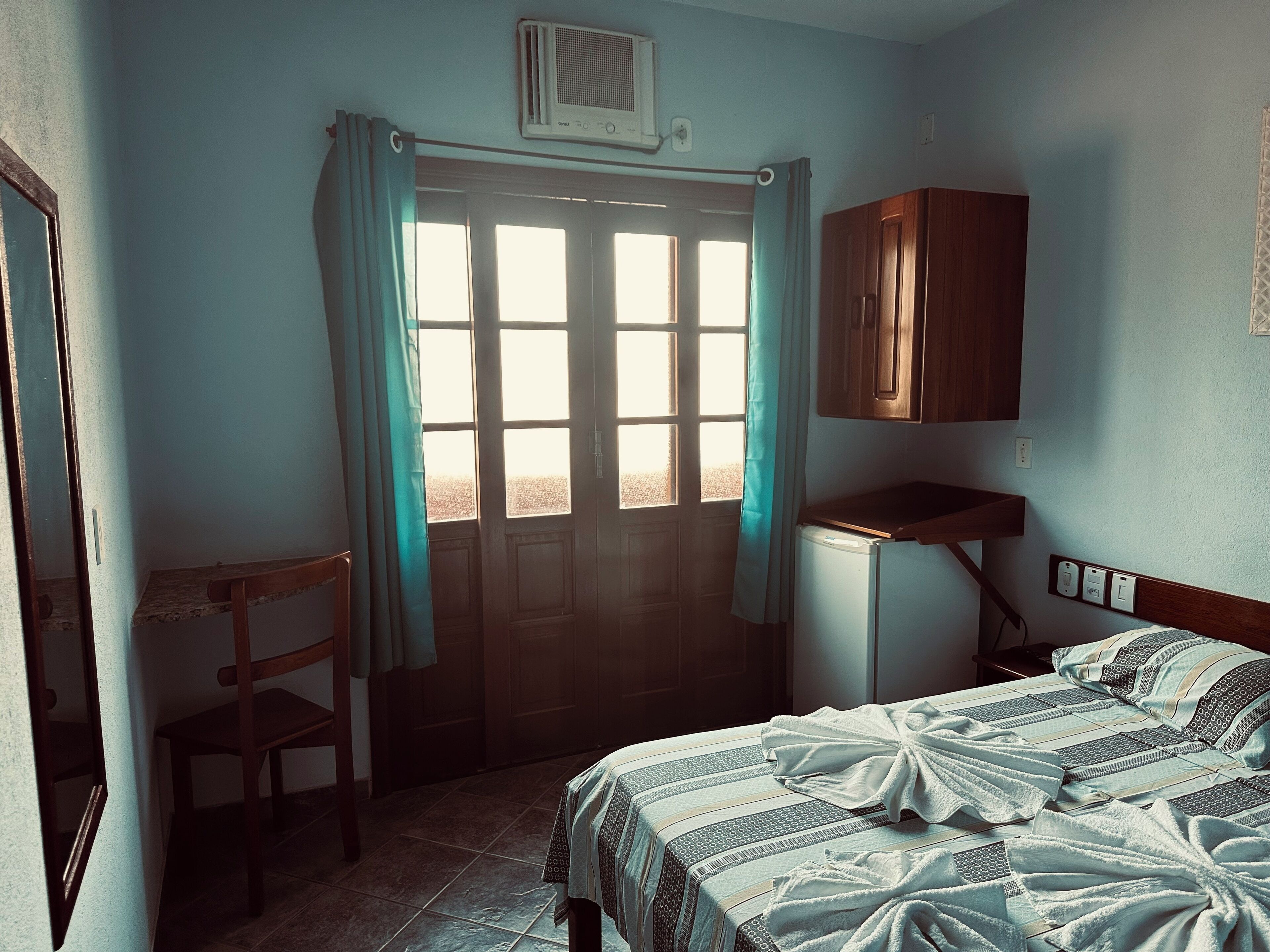 Ein Schlafzimmer mit einem Bett, einem Sessel, einem Schreibtisch und einem Fenster mit Vorhängen.