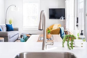 A modern kitchen with a stainless steel sink, a flat-screen TV mounted above it, and a dining area with a table and chairs.