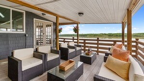 Ett takförsett utomhusområde med sittplatser, möbler i rotting, ett träbord och utsikt över en sjö.