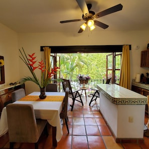 Un comedor con una mesa, sillas, un ventilador de techo y vistas a la vegetación exterior.