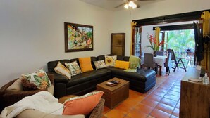 A living room with a black sofa, a wicker chair, a coffee table, and a painting on the wall. - Casa Tortuga @ Selva Romantica (Puerto Vallarta)