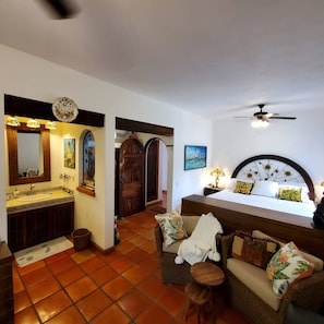 A bedroom with a bed, a nightstand, a lamp, a ceiling fan, a bathroom with a sink, mirror, and decorative lights.