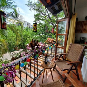 A balcony with a wicker chair, a table with a bottle and glass, and a railing decorated with colorful paper lanterns.