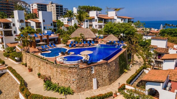 A resort with a large central pool surrounded by lounge chairs and umbrellas, set against a backdrop of buildings and a clear sky. - Casa Tortuga @ Selva Romantica (Puerto Vallarta)